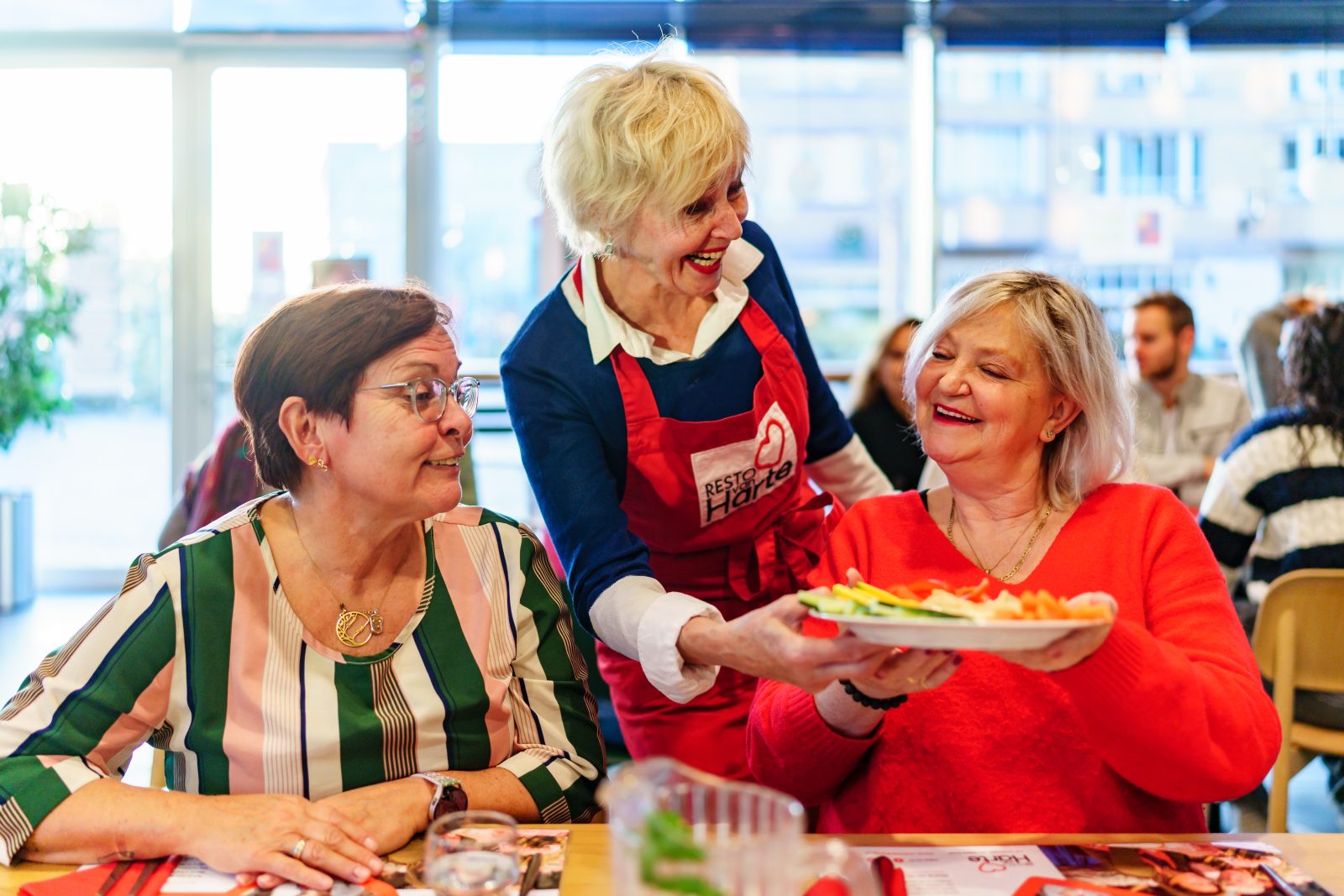 Vrijwilligster Resto VanHarte geeft twee oudere dames een bord aan